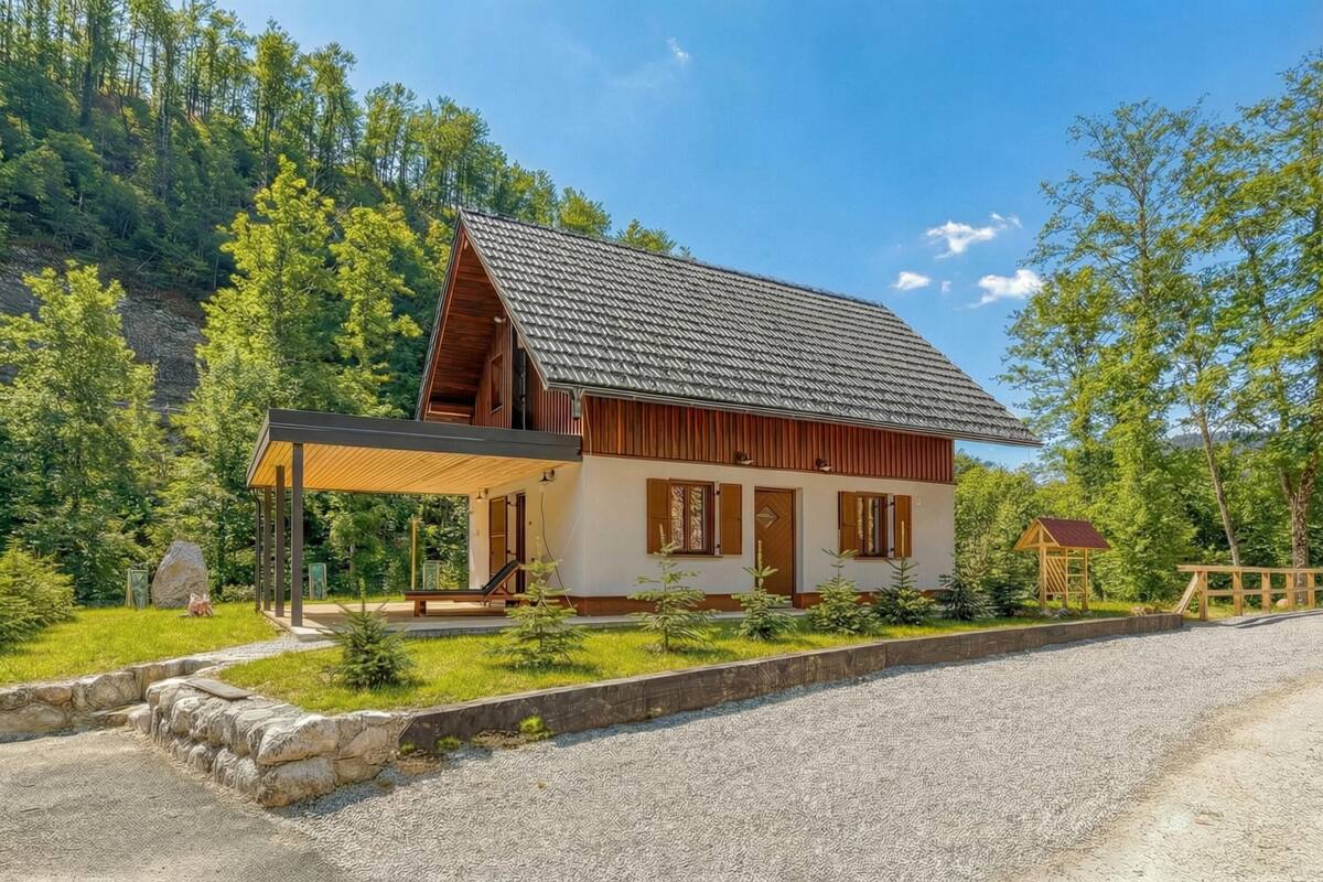 Ein zweistöckiges Holzhaus mit einer überdachten Veranda, umgeben von einem Schotterhof und üppiger Bepflanzung.