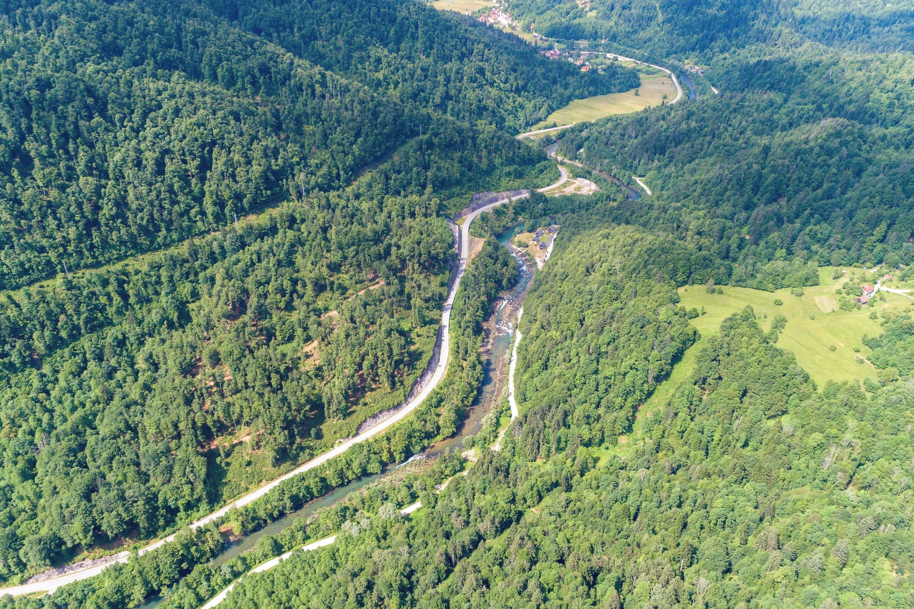 Vista aérea de un río sinuoso que atraviesa un valle densamente arbolado, con una carretera que serpentea a su lado.