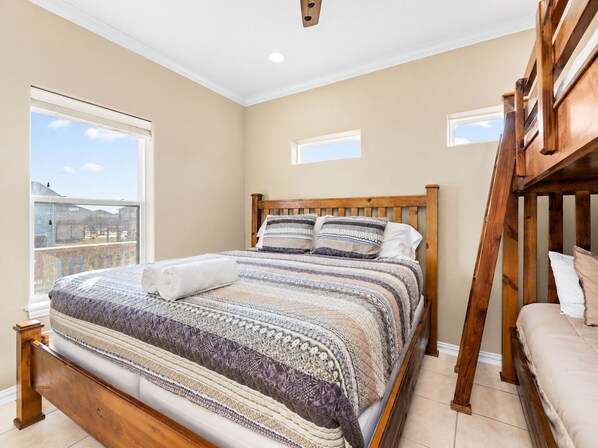 A bedroom with a wooden bed, a view of the city, and a balcony. - Steps to Beach | 4BR | Deck + Ocean Views (Crystal Beach)