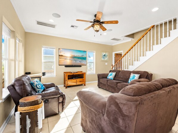 A living room with a brown leather sofa, a wooden coffee table, a ceiling fan, a TV, and a staircase.