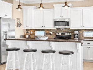 A modern kitchen with white cabinetry, a stainless steel refrigerator, a microwave, a stove, and three bar stools. - Steps to Beach | 4BR | Deck + Ocean Views (Crystal Beach)