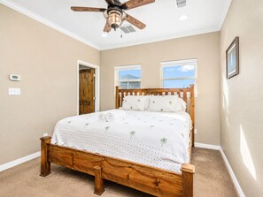 A bedroom with a wooden bed, a ceiling fan, and a view of the outdoors through two windows.