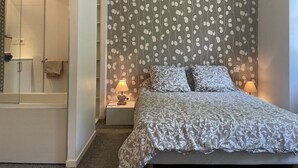 A bedroom with a bed, nightstands, a lamp, and a shower area.