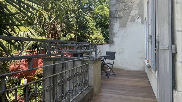 A balcony with a wooden floor, metal railing, and a chair.