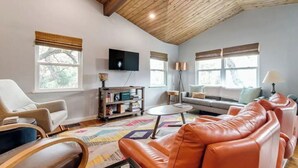 A spacious living room with a high wooden ceiling, a large sofa, a coffee table, and a bookshelf. - Mid Century Charmer, oversize fenced corner yard, fire pit,hot tub, pet friendly (Fredericksburg)