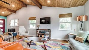 A living room with a wooden ceiling, a television, a sofa, a chair, a coffee table, and a bookshelf. - Mid Century Charmer, oversize fenced corner yard, fire pit,hot tub, pet friendly (Fredericksburg)