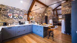 A kitchen with blue cabinets, a stone wall, and a wooden ceiling. There are three framed signs on the wall, a clock, and a coffee machine on the counter. - The Mill @ Atlow Mill (Atlow)