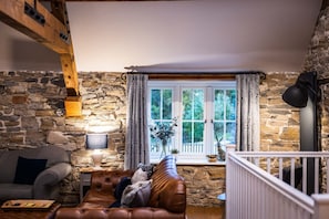 Relax in this inviting living room with a leather sofa, armchair, and side table, surrounded by a wooden beam structure and a stone wall.