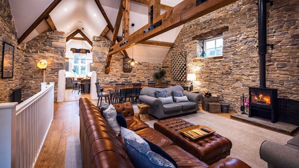 A cozy interior with a stone wall, wooden beams, a fireplace, and a seating area with a sofa and ottoman. - The Mill @ Atlow Mill (Atlow)