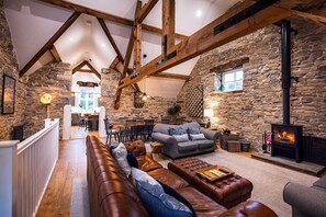 Un interior acogedor con pared de piedra, vigas de madera, chimenea y zona de estar con sofá y reposapiés.