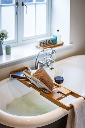Ein Badezimmer mit einer Badewanne, einem Holztablett mit Büchern und einem Glas Rotwein, einem Handtuch und einem Fenster mit Blick.