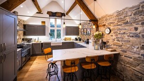 A kitchen with a large island, stone wall, and wooden beams. - The Mill @ Atlow Mill (Atlow)