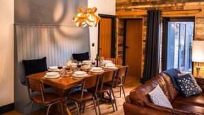 A dining area with a wooden table set for four, a brown leather sofa, and a wooden ceiling with exposed beams. - The Cow Shed @ Atlow Mill (Atlow)