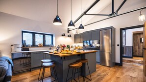 A modern kitchen with a central island, bar stools, and a large refrigerator. - The Cow Shed @ Atlow Mill (Atlow)