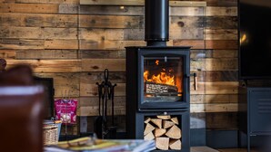 A cozy room with a wood-burning stove, two wall-mounted lights, a TV, and a seating area with a table and chairs. - The Cow Shed @ Atlow Mill (Atlow)