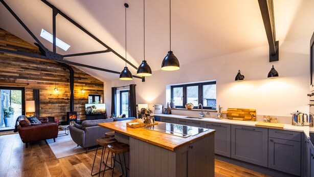 A modern kitchen with a central island, wooden flooring, and pendant lighting. - The Cow Shed @ Atlow Mill (Atlow)