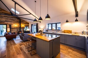 A modern kitchen with a central island, wooden flooring, and pendant lighting. - The Cow Shed @ Atlow Mill (Atlow)