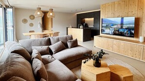 Una sala de estar moderna con un sofá seccional grande, una mesa de centro de madera y un televisor de pantalla plana montado en una pared de madera.