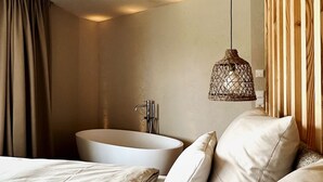 Una habitación de hotel moderna con una cama grande, una bañera y una lámpara colgante.