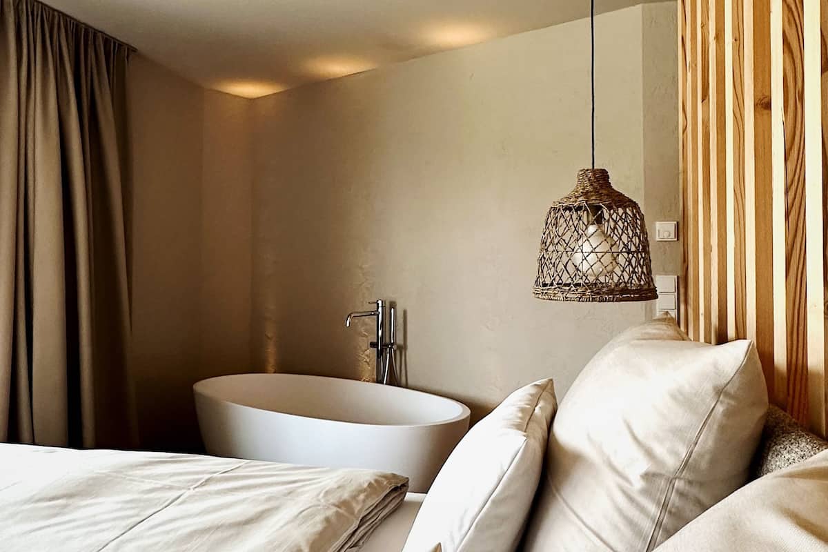 Une chambre d’hôtel moderne avec un grand lit, une baignoire et un luminaire suspendu.