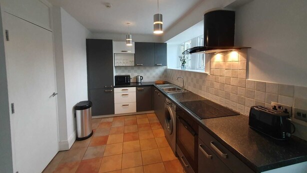 A modern kitchen with a dishwasher, sink, and a black range hood. - Cosy, Central Apartment Skipton (Skipton)