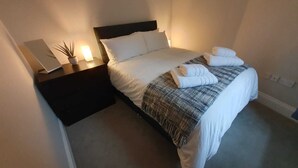 A neatly made bed with white linens and a grey blanket, a bedside table with a lamp, and a laptop. - Cosy, Central Apartment Skipton (Skipton)