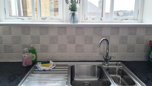 A kitchen with a stainless steel sink, a window above it, and a vase with flowers on the windowsill. - Cosy, Central Apartment Skipton (Skipton)
