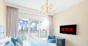 Een hotelkamer met een groot bed, een aan de muur bevestigde televisie, een klein tv-tafeltje, een stoel en uitzicht op de stadshemel via grote ramen.