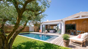 En baghave med swimmingpool, træterrasse, udendørs møbler og et stort træ.