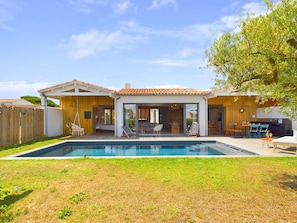 Ein modernes Haus mit Schwimmbecken, Holzterrasse und Sitzgelegenheiten im Freien.