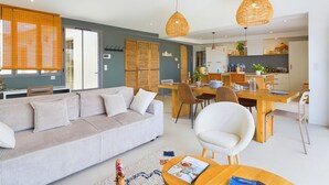 En moderne stue med sofa, spisebord og stole. Der er et køkkenområde med skabe og en bordplade.