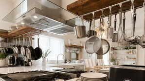 Una cocina moderna con electrodomésticos de acero inoxidable, ollas colgadas y encimera blanca.