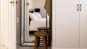 Un dormitorio con cama, espejo, armario y un taburete pequeño.