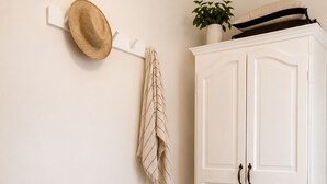 Una habitación con un armario blanco, un tapete tejido, un sombrero en un perchero de pared y una toalla a rayas.