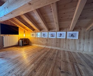 Une pièce aux murs lambrés, avec un plafond en pente, un radiateur, une petite table sur laquelle se trouve une lampe, et des tableaux encadrés accrochés au mur.