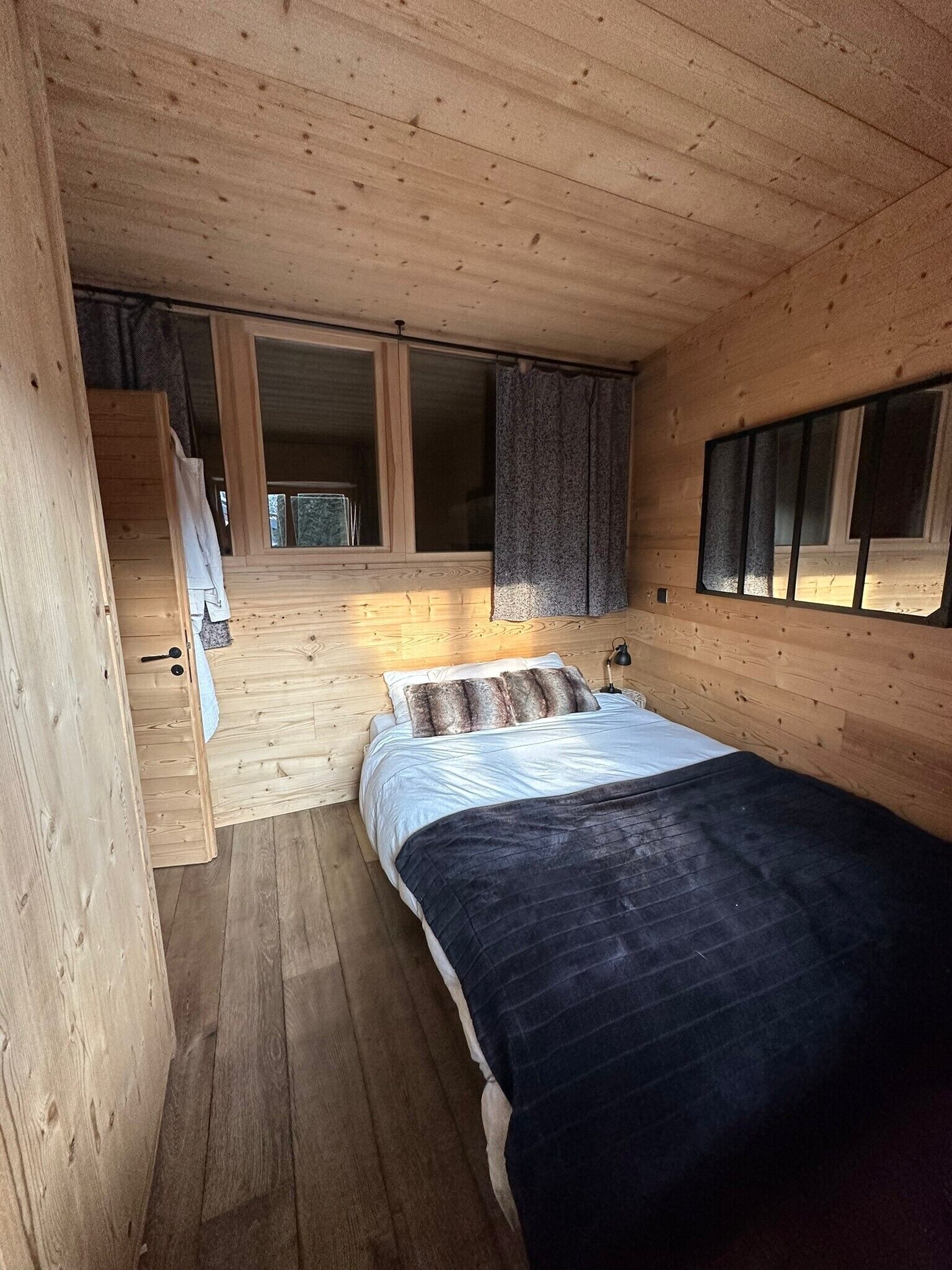 Un dormitorio de cabaña de madera con una cama, una ventana con cortinas y una escalera que lleva a un nivel superior.