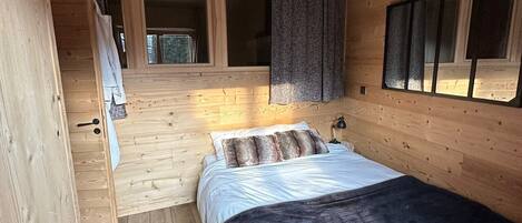 Un dormitorio de cabaña de madera con una cama, una ventana con cortinas y una escalera que lleva a un nivel superior.