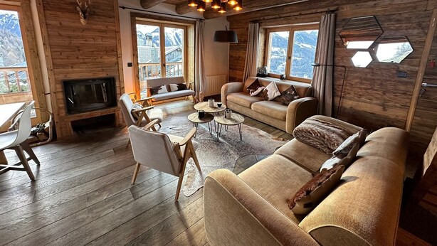 A cozy log cabin interior with a sofa, chairs, a small table, and a fireplace.