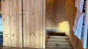 A wooden interior with a sauna area, wooden flooring, and towels hanging on a rack.