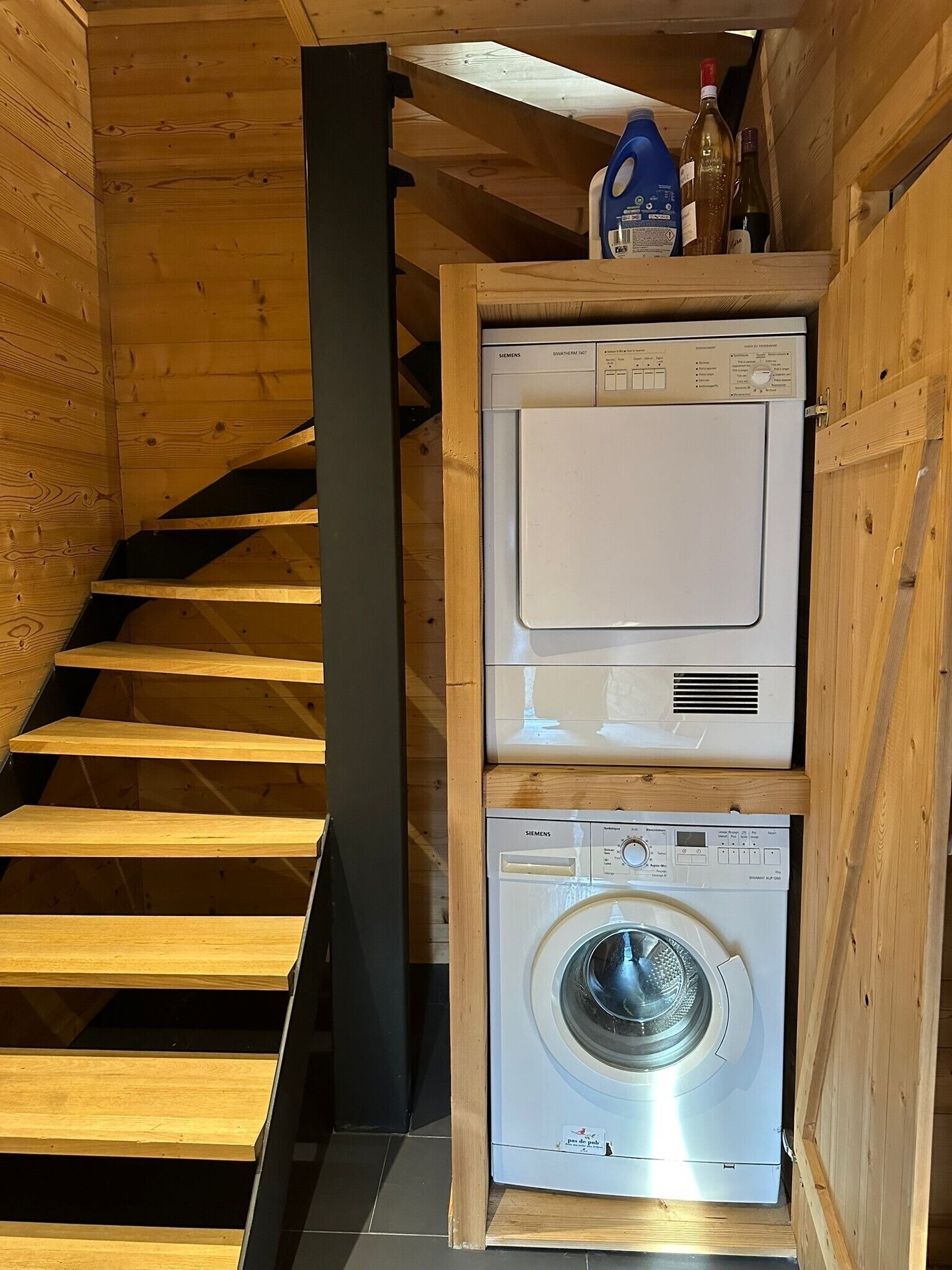 Eine Holztreppe führt zu einem Waschraum mit gestapelten Waschmaschinen.