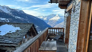 A wooden deck with a bench, stone walls, and a view of snow-capped mountains.