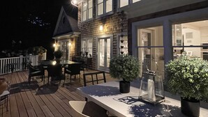 Une maison à deux étages dotée d’une terrasse, d’un éclairage extérieur et de plantes en pot.