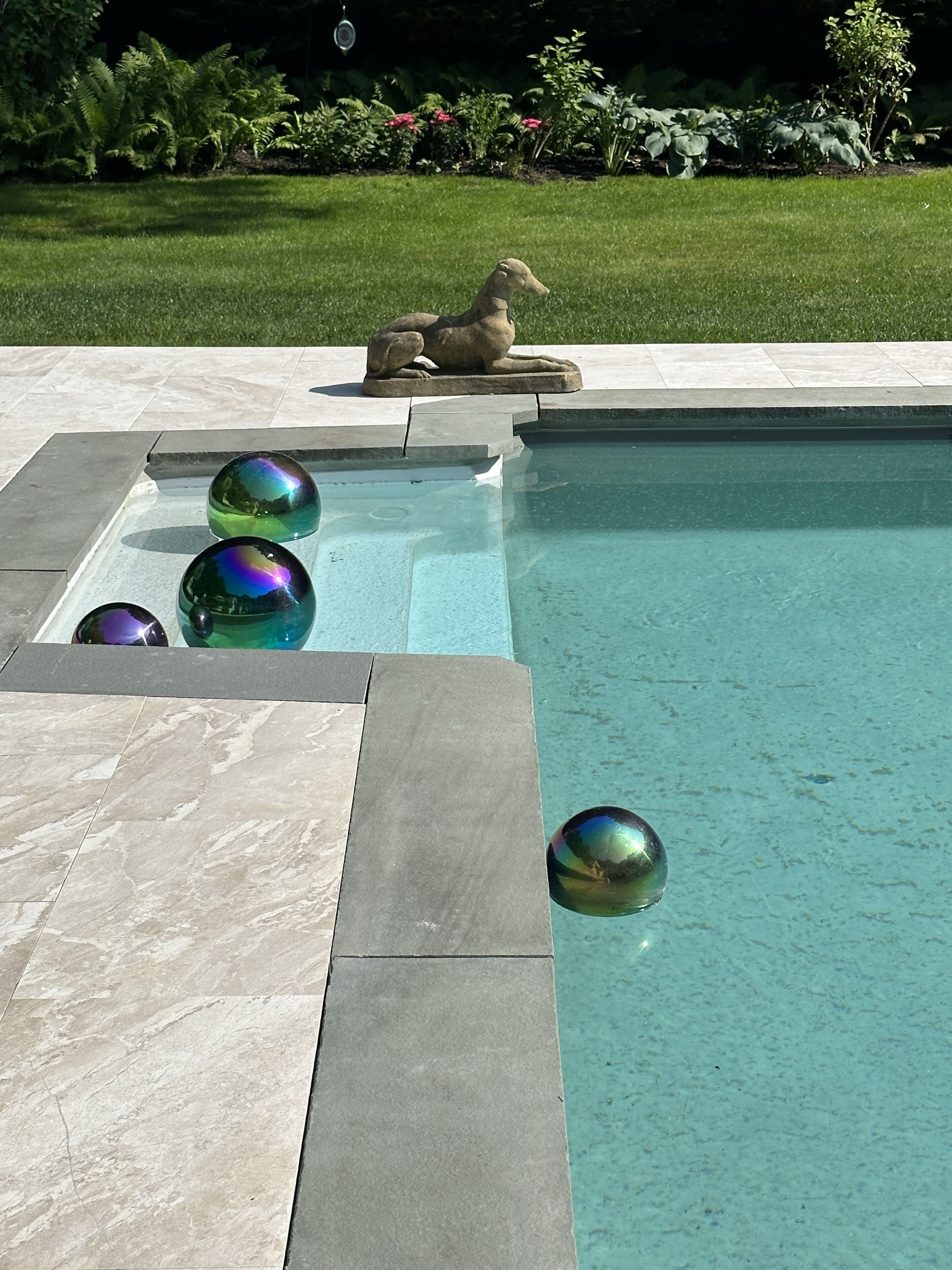 A swimming pool with three iridescent spheres and a stone sculpture.