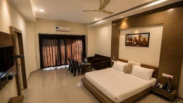 Habitación de hotel con cama, escritorio, silla, televisor y aire acondicionado.