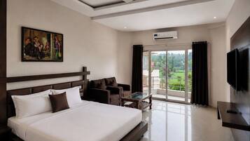 A hotel room with a large bed, a ceiling fan, a TV, a painting, and a balcony with a view.