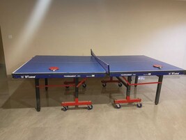 Dos mesas de ping pong Vixen Tournament Pro con ruedas, ubicadas en una habitación con pared lisa y suelo de baldosas.