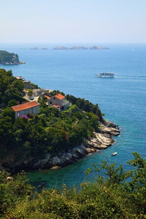 A coastal property with a red-roofed building, a boat in the water, and a clear view of the sea. - Sunset Oasis (Dubrovnik)