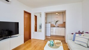A modern living room with a flat-screen TV, a white sofa, and a coffee table with books and a decorative item. - Sunset Oasis (Dubrovnik)