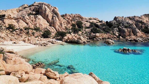 Eine zerklüftete Küstenlinie mit klarem türkisblauem Wasser und einem Sandstrand.