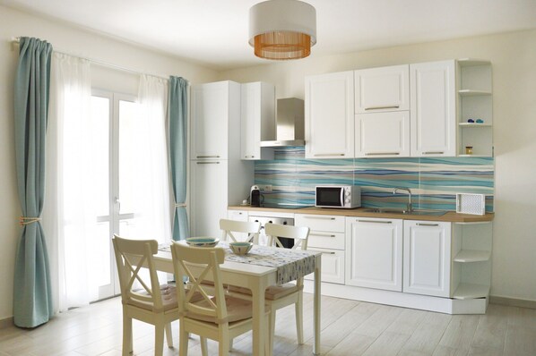 A modern kitchen with white cabinets, a microwave, and a striped backsplash. There is a dining table with chairs and a window with curtains.